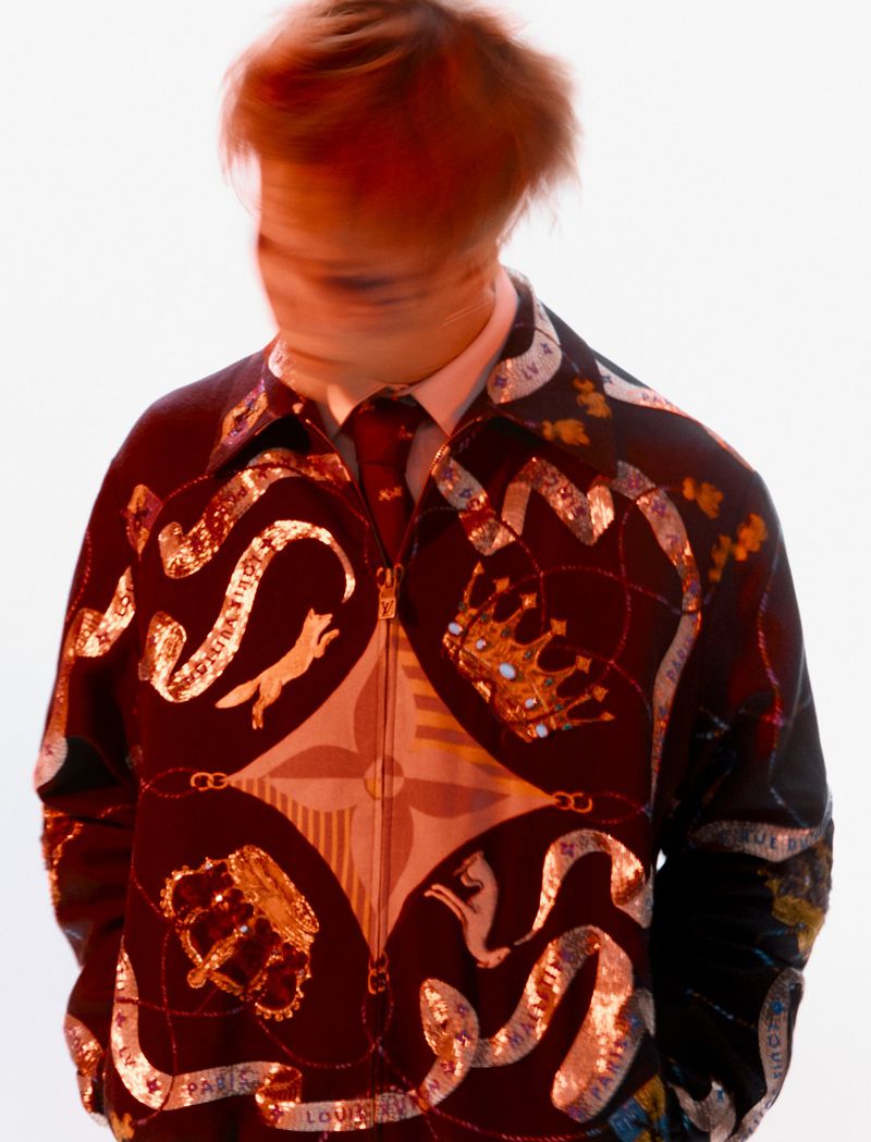 Blurred portrait of an adult wearing a patterned jacket, tie, and collared shirt against a stark white background.