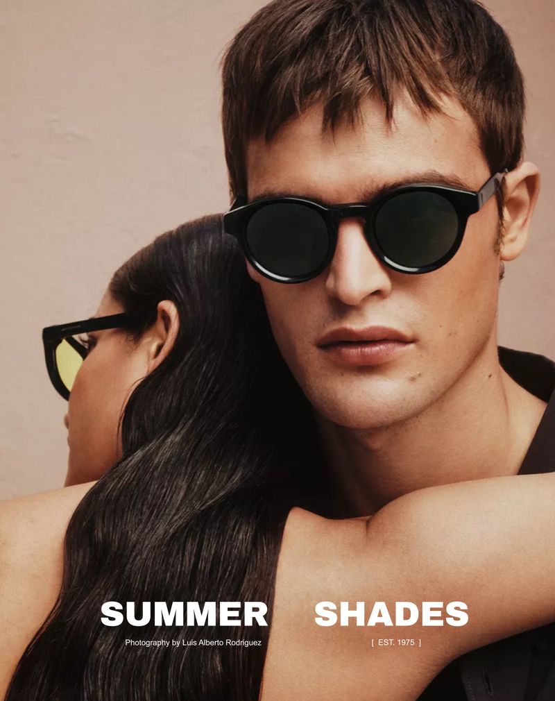 Close-up portrait of a man wearing black sunglasses with another person leaning in from behind wearing yellow sunglasses for Zara.
