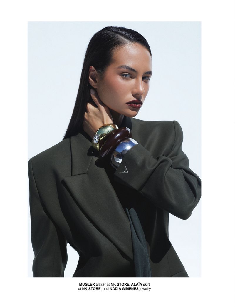 Mari Brechane wearing an oversized olive blazer and layered chunky bangles against a clean white backdrop.