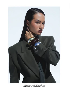 Mari Brechane wearing an oversized olive blazer and layered chunky bangles against a clean white backdrop.