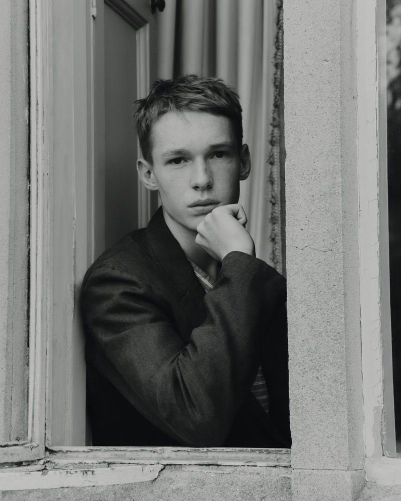 Portrait of a young adult male with short red hair sitting in a window, wearing a suit jacket, looking thoughtfully at the camera.