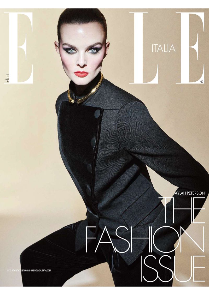 Elle Italia fashion editorial cover featuring a model with red lipstick, wearing a black suit and gold necklace on a tan background.