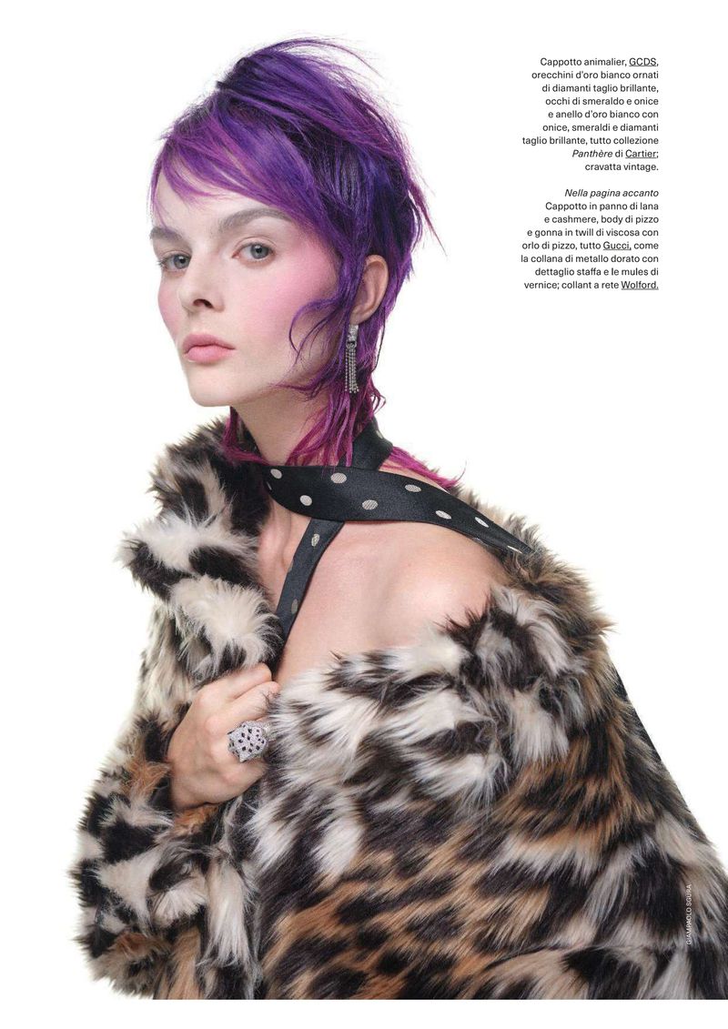 Elegant woman with purple hair poses in a studio wearing a leopard print fur coat with a black and white polka dot strap top.