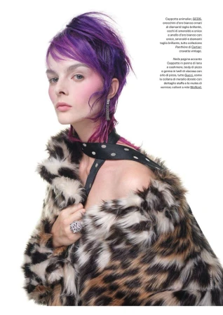 Elegant woman with purple hair poses in a studio wearing a leopard print fur coat with a black and white polka dot strap top.