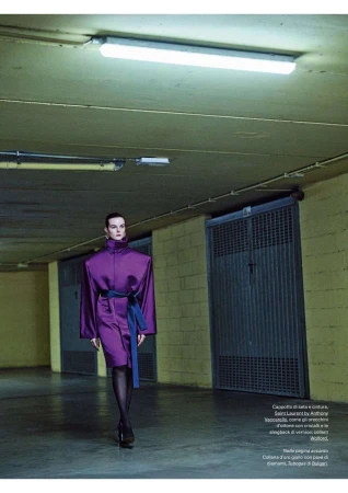 Fashion editorial image of a woman walking in a purple dress with a blue belt, posing in an indoor underground parking garage.