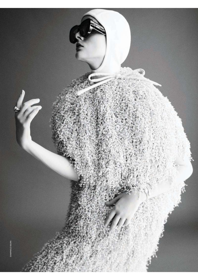 A monochrome fashion shot features a woman in a fringed dress, complemented by a head covering and sunglasses, against a grey backdrop.