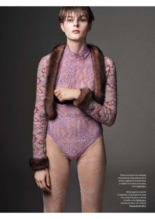 Fashion editorial shot of a model wearing a lilac lace bodysuit, patterned sheer tights, and a dark fur stole in a studio setting.