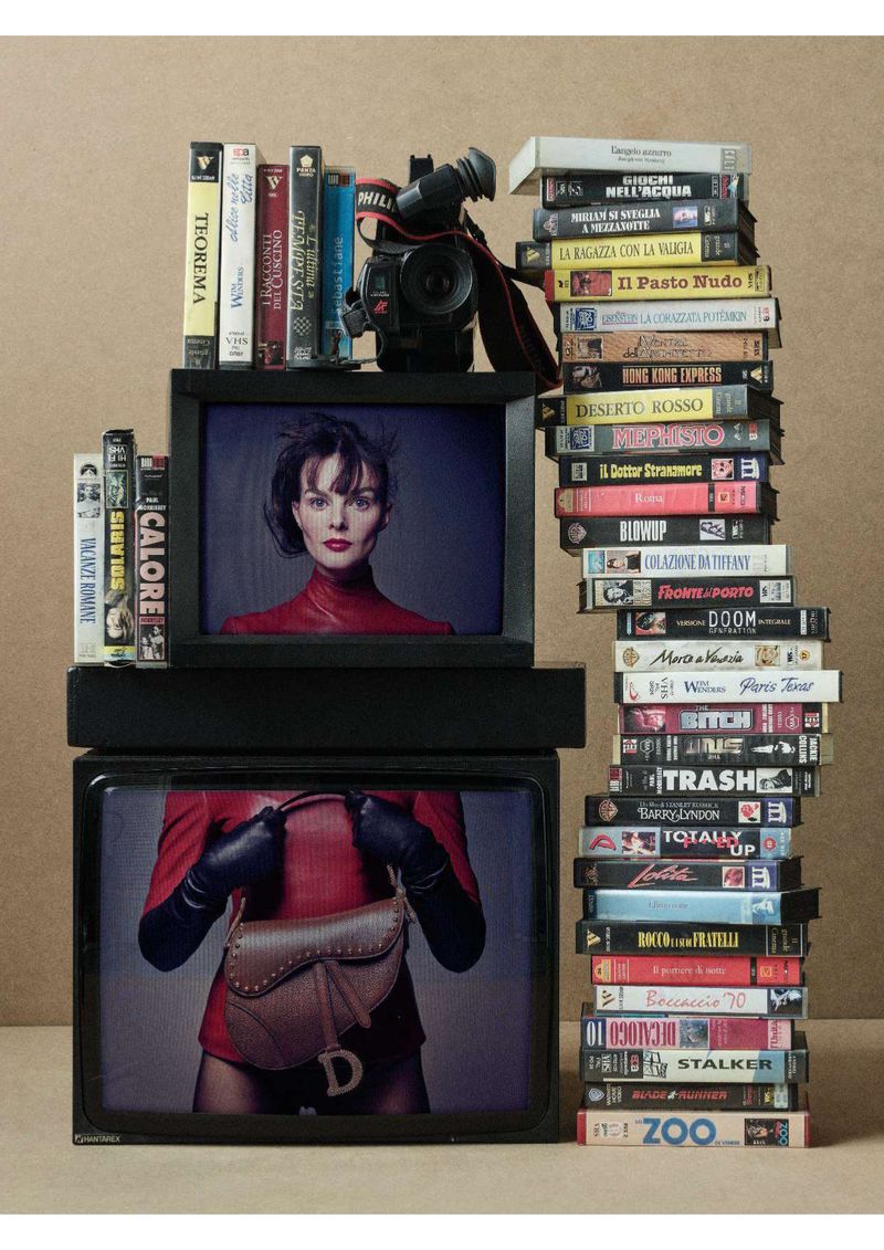 Fashion editorial featuring a vintage television set stacked with VHS tapes, displaying an image of a model in a red outfit.