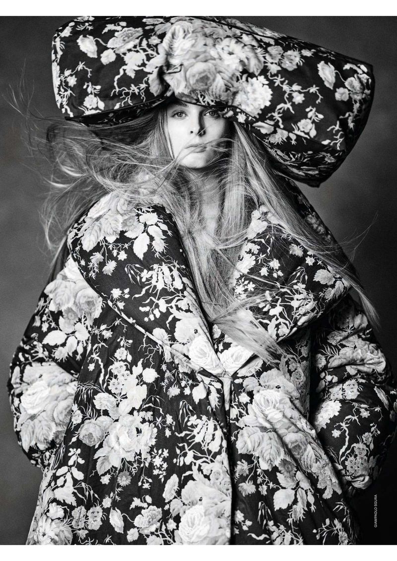 Fashionable adult female poses in monochrome floral print hat and jacket. Studio shot with dramatic contrast and flowing hair.