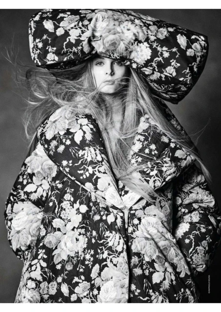Fashionable adult female poses in monochrome floral print hat and jacket. Studio shot with dramatic contrast and flowing hair.