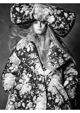 Fashionable adult female poses in monochrome floral print hat and jacket. Studio shot with dramatic contrast and flowing hair.