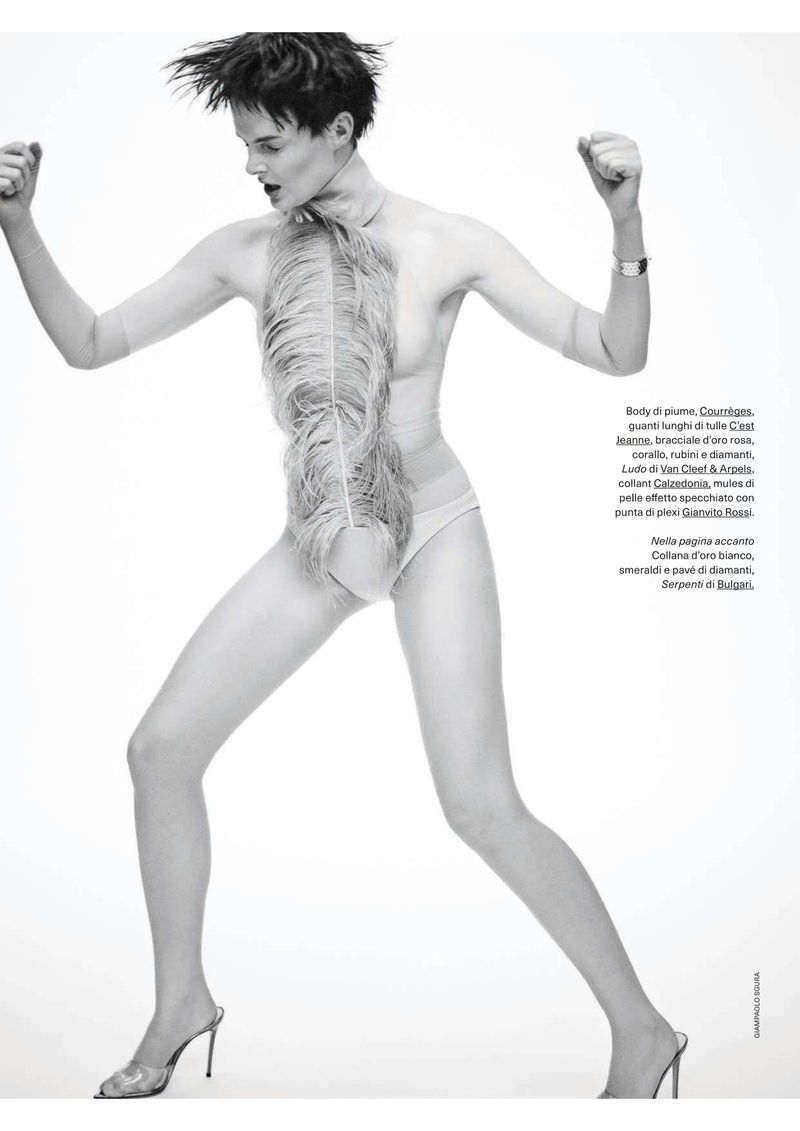 A fashion shot featuring a slender adult woman with short dark hair in a light-colored bodysuit, posing against a bright backdrop.