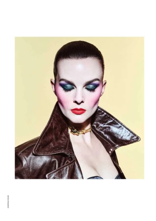 Fashion portrait of a woman with dramatic makeup and a brown leather jacket against a yellow background in a studio setting.