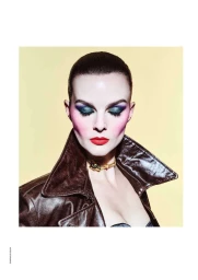 Close-up portrait of model Aylah Peterson wearing dramatic eye makeup and a brown leather jacket against a pale yellow background.