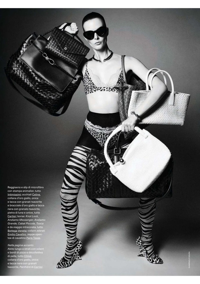 Model wearing leopard print lingerie and sunglasses holding multiple leather handbags in a black and white editorial shoot