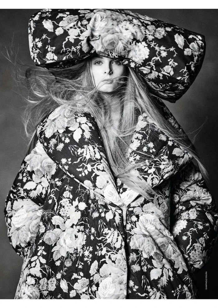 Model Aylah Peterson wearing an oversized monochrome floral quilted coat and matching structured headpiece against a dark studio backdrop.