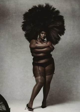 Full-length studio shot of a black woman in lingerie and heels, wearing a voluminous afro hairstyle, arms crossed, and expressionless.