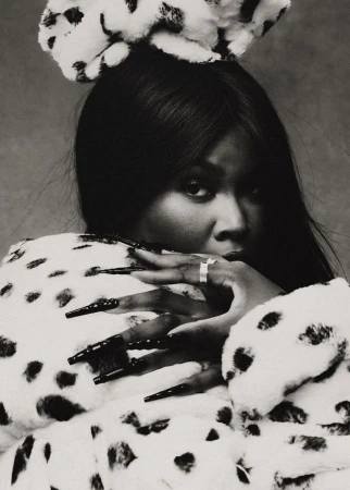 Black and white portrait of a woman with long black nails, wearing a dalmatian print coat and bow, gazing at the camera.