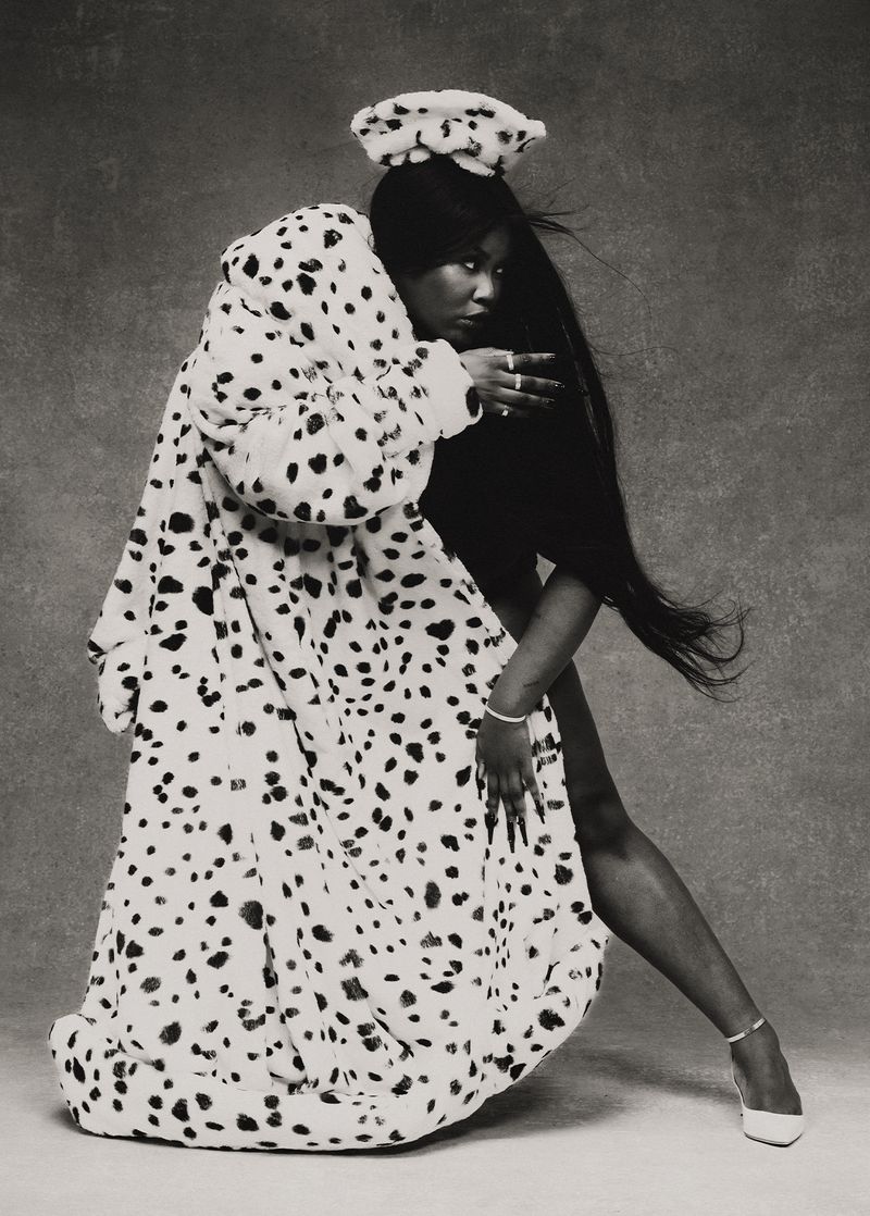 Singer Yseult posing dynamically in an oversized dalmatian-print faux fur coat and matching beret against a textured studio backdrop.