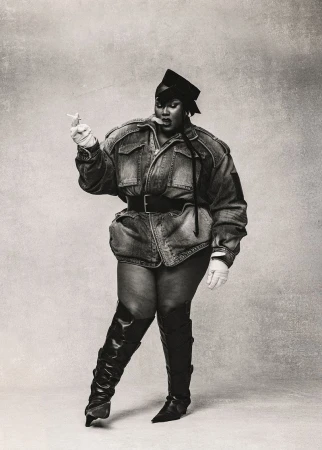 A portrait captures a plus-size African-American woman wearing a denim outfit and black leather boots, smoking against a neutral background.