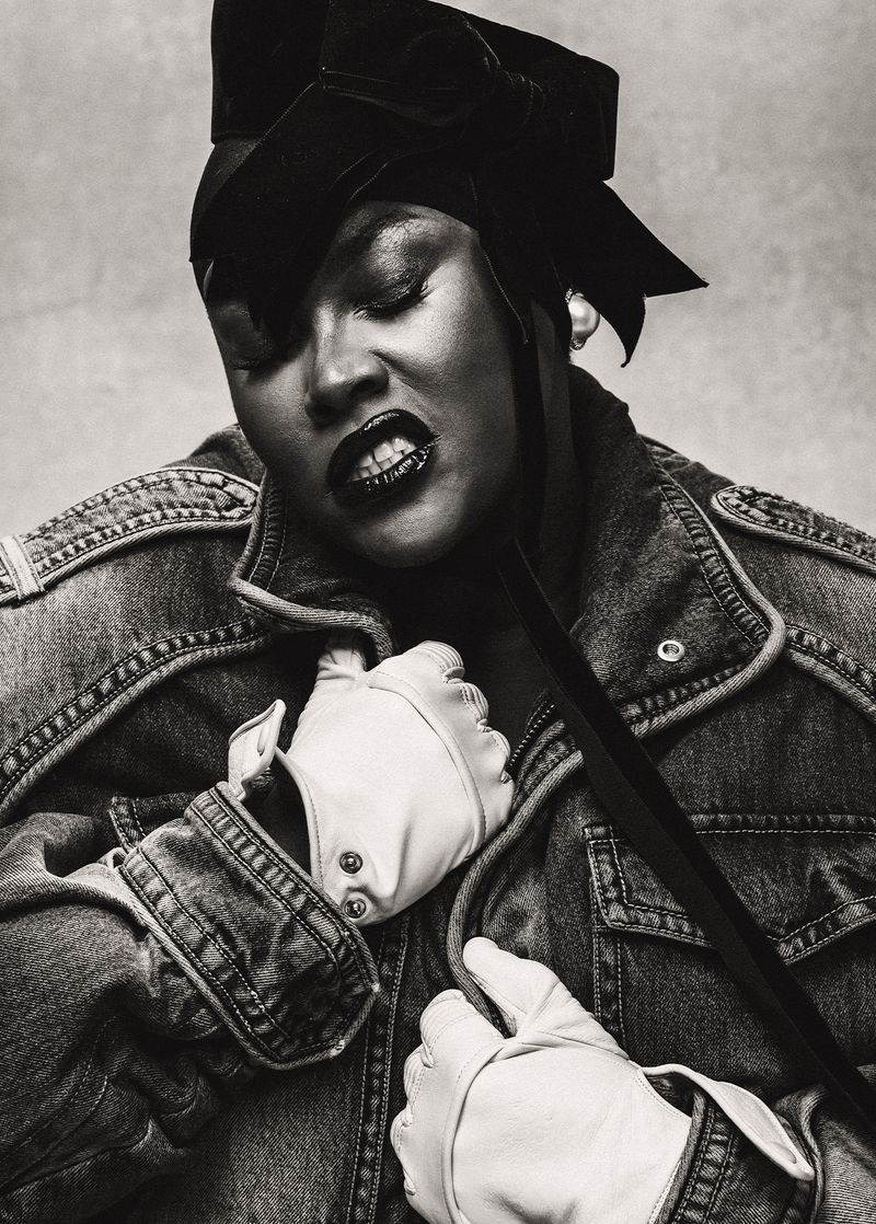 Black and white portrait of Yseult wearing a denim jacket, black velvet bow headpiece, and white leather driving gloves.