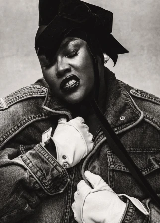 Black and white portrait of Yseult wearing a denim jacket, black velvet bow headpiece, and white leather driving gloves.