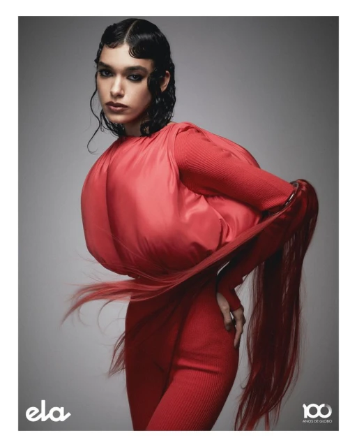 Fashion portrait of a woman with dark hair in a sculptural red dress against a grey studio backdrop in a vertical composition.