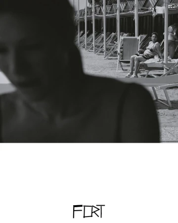 Black and white photo of a woman sitting on a beach chair, with other chairs and shelters in the background and another person in foreground.