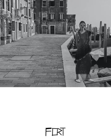 Black-and-white fashion shot of a woman with sunglasses in a sleeveless outfit, posing on a Venice canal-side walkway with buildings.
