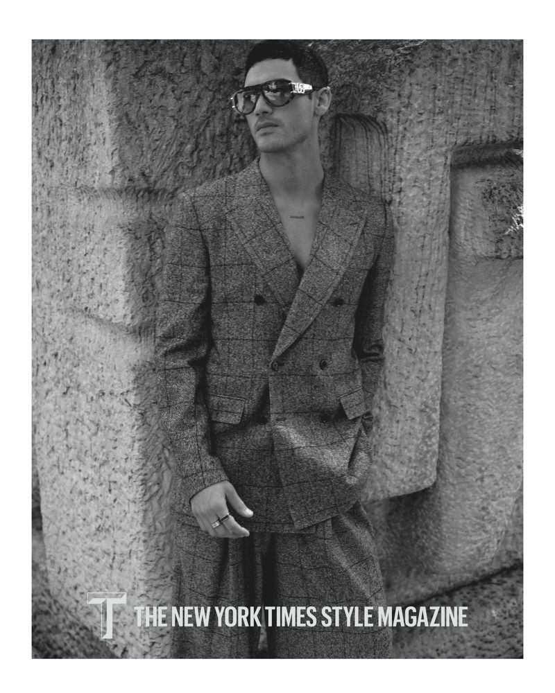Monochrome portrait of a male model in a checkered suit with sunglasses, posing against a textured wall for The New York Times Style Magazine.