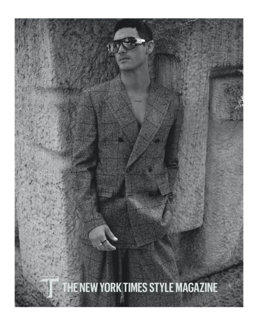 Monochrome portrait of a male model in a checkered suit with sunglasses, posing against a textured wall for The New York Times Style Magazine.