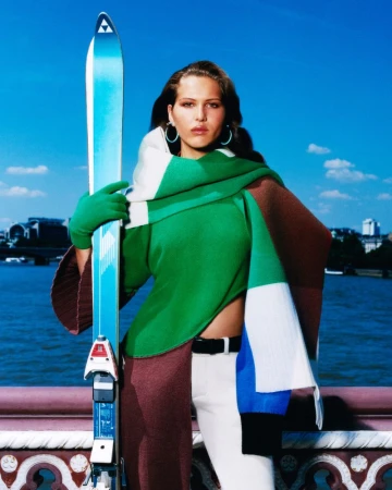 Adult female outdoor portrait with a pair of Fischer skis, wearing a bright color-blocked outfit with a river and skyline backdrop.