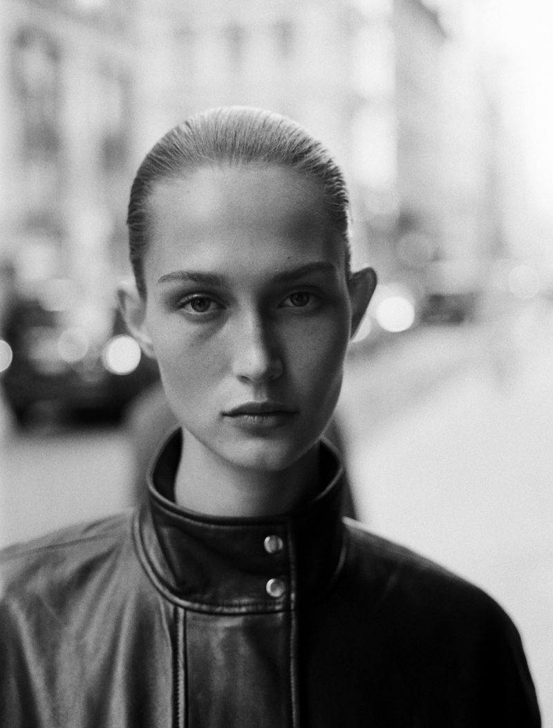 Black and white portrait of model Vika Evseeva wearing a high collar black leather jacket on an urban street.