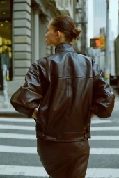 Model standing on a city street crossing wearing a dark leather jacket seen from behind