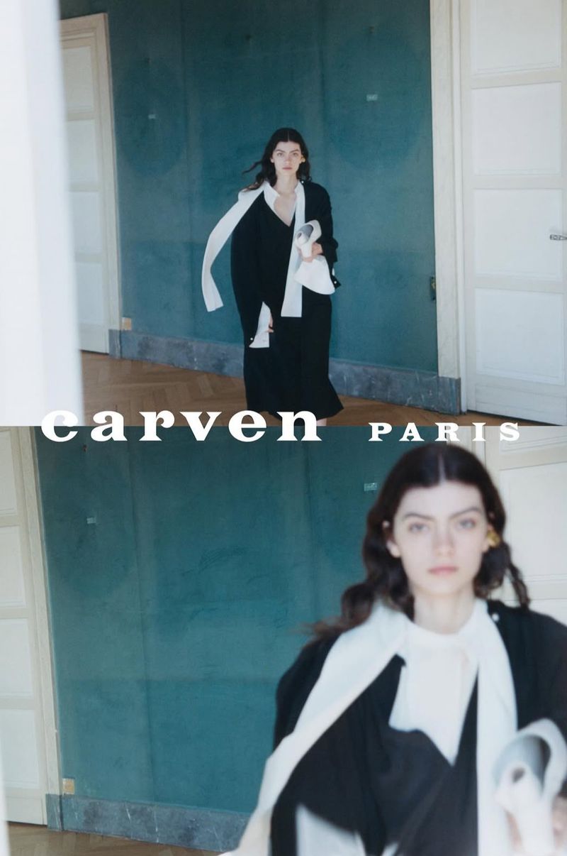 Model Flavie Sammartano in a black coat with an elongated white scarf against a teal wall for Carven Paris.