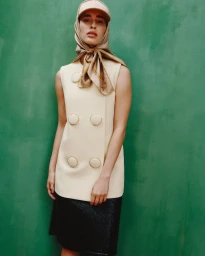 Model Lotte Bella Tscharntke wearing a cream double-breasted tunic and silk headscarf against a green studio backdrop.