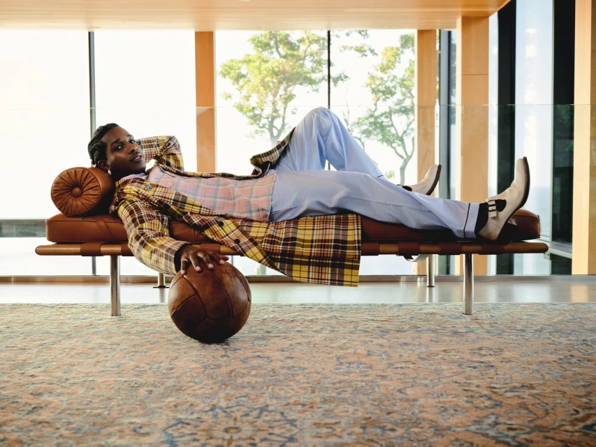 Adult male relaxing on a modern leather daybed in a bright, minimalist room with a vintage soccer ball and large windows overlooking trees.