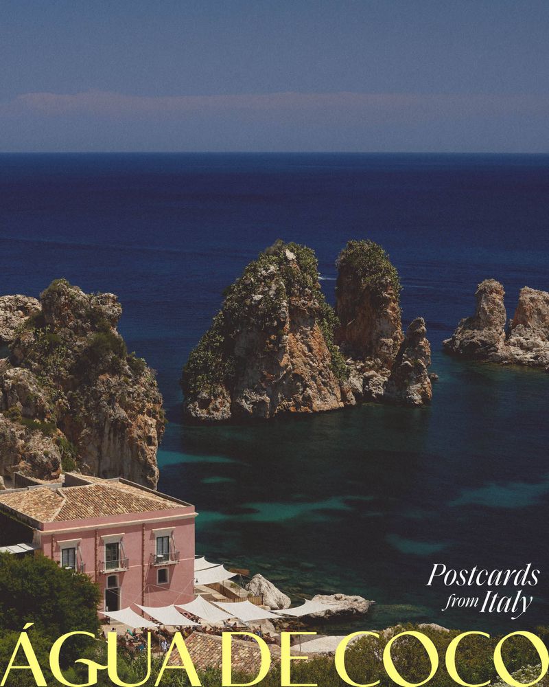 Coastal scene in Italy with rocky cliffs, turquoise water, and a pink building with a tan roof, captured in a picturesque, sunny landscape.