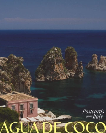 Coastal scene in Italy with rocky cliffs, turquoise water, and a pink building with a tan roof, captured in a picturesque, sunny landscape.