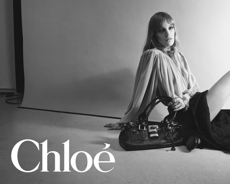 Black and white fashion shot of a woman posing with a leather handbag in a studio setting, featuring the Chloé brand logo.