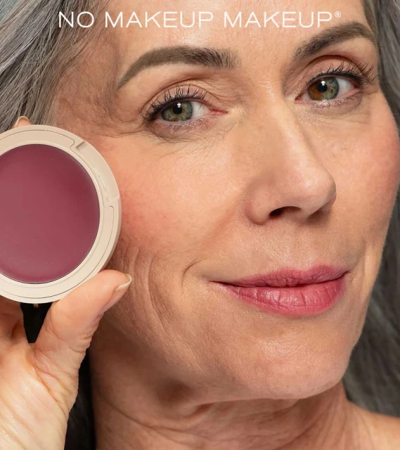 Mature woman showcases a red blush makeup product in its container, emphasizing natural beauty and age-positive cosmetics.