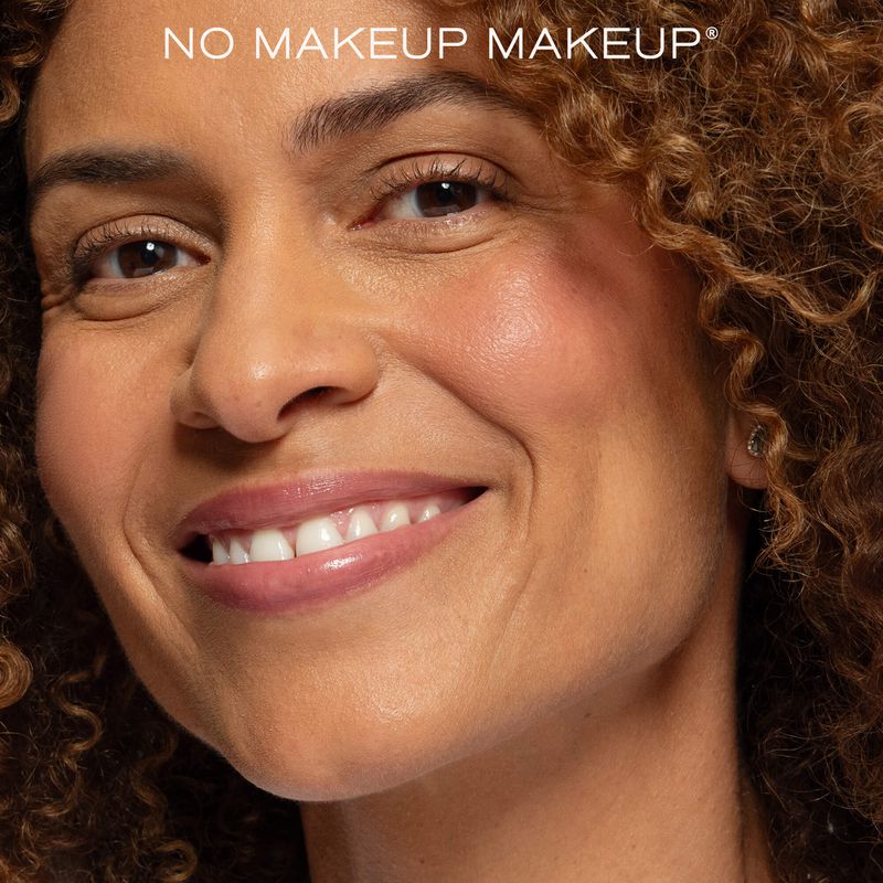 Close-up beauty portrait of a smiling woman with curly brown hair and radiant natural makeup.