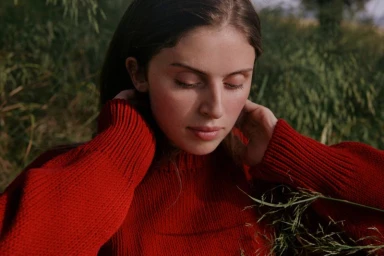 Woman wearing a bright red ribbed knit sweater outdoors with tall green grass in the background