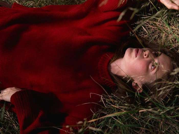 Woman wearing a chunky red knit sweater lying on grass outdoors