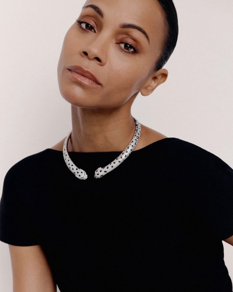 Portrait of Zoe Saldana wearing a silver panther choker necklace, posing against a pale background with a black top.