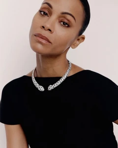 Zoe Saldaña wearing a Cartier diamond panther collar necklace and a black short-sleeved top against an off-white background.