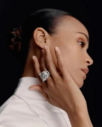 Profile portrait of Zoe Saldana wearing a Cartier diamond panther ring and white top against a black background