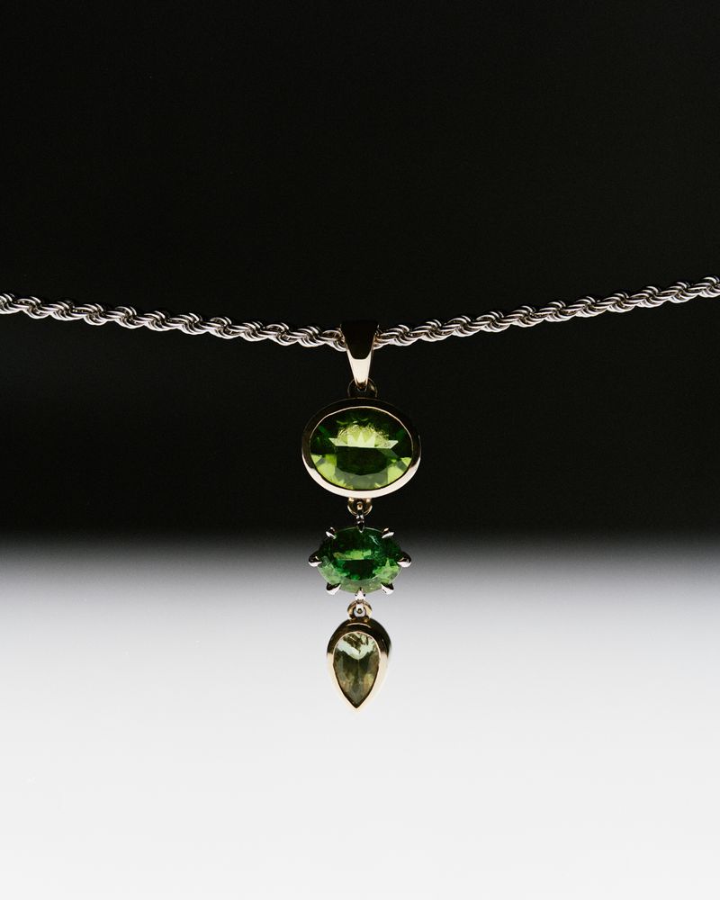 Elegant necklace with green gemstones on a silver chain against a dark to light gradient background, jewellery photography.