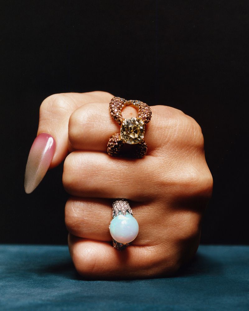 Close-up of a woman's fist adorned with two statement rings against a dark backdrop, emphasizing the jewelry's design and vibrant colors.