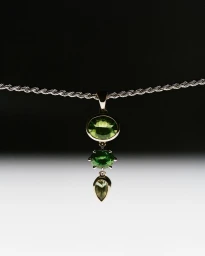 Three-tier green gemstone pendant suspended from a twisted silver rope chain necklace against a high-contrast gradient background.